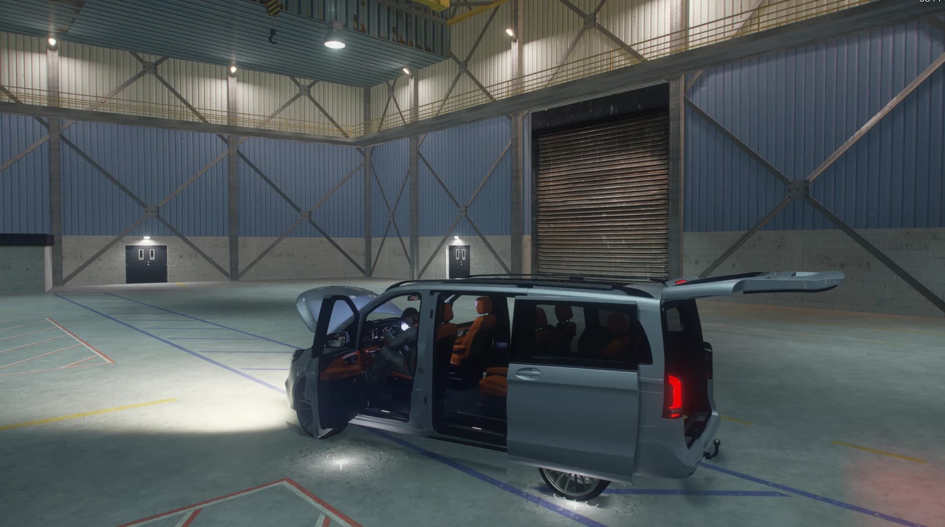 Silver van in a warehouse with the hood, sliding door and tailgate open showing the orange lounge seats and a driver at the wheel