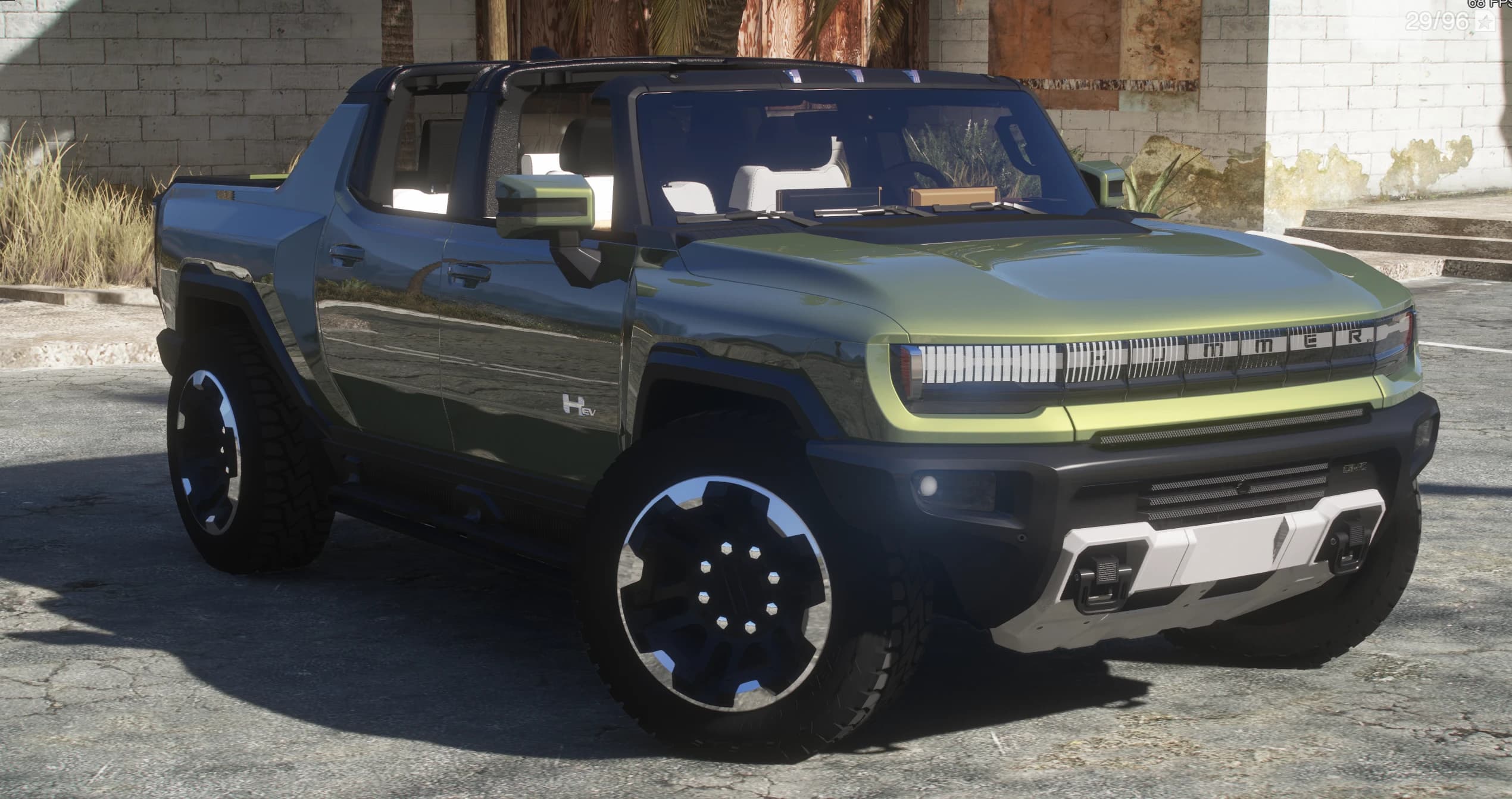 Two-tone green GMC Hummer EV pickup with the roof panels removed, parked by a derelict brick building, with the HUMMER light-bar grille and chunky off-road tyres