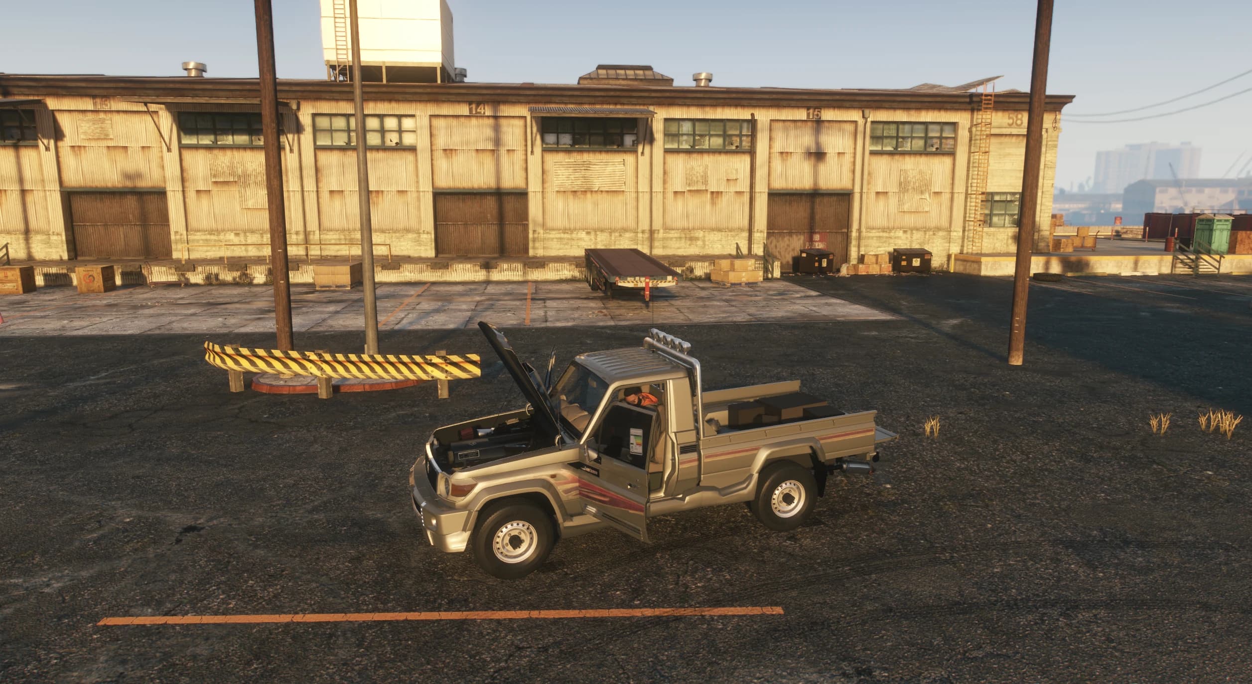 Side view with the hood and doors open showing the engine bay, a driver seated inside and cargo boxes loaded in the bed