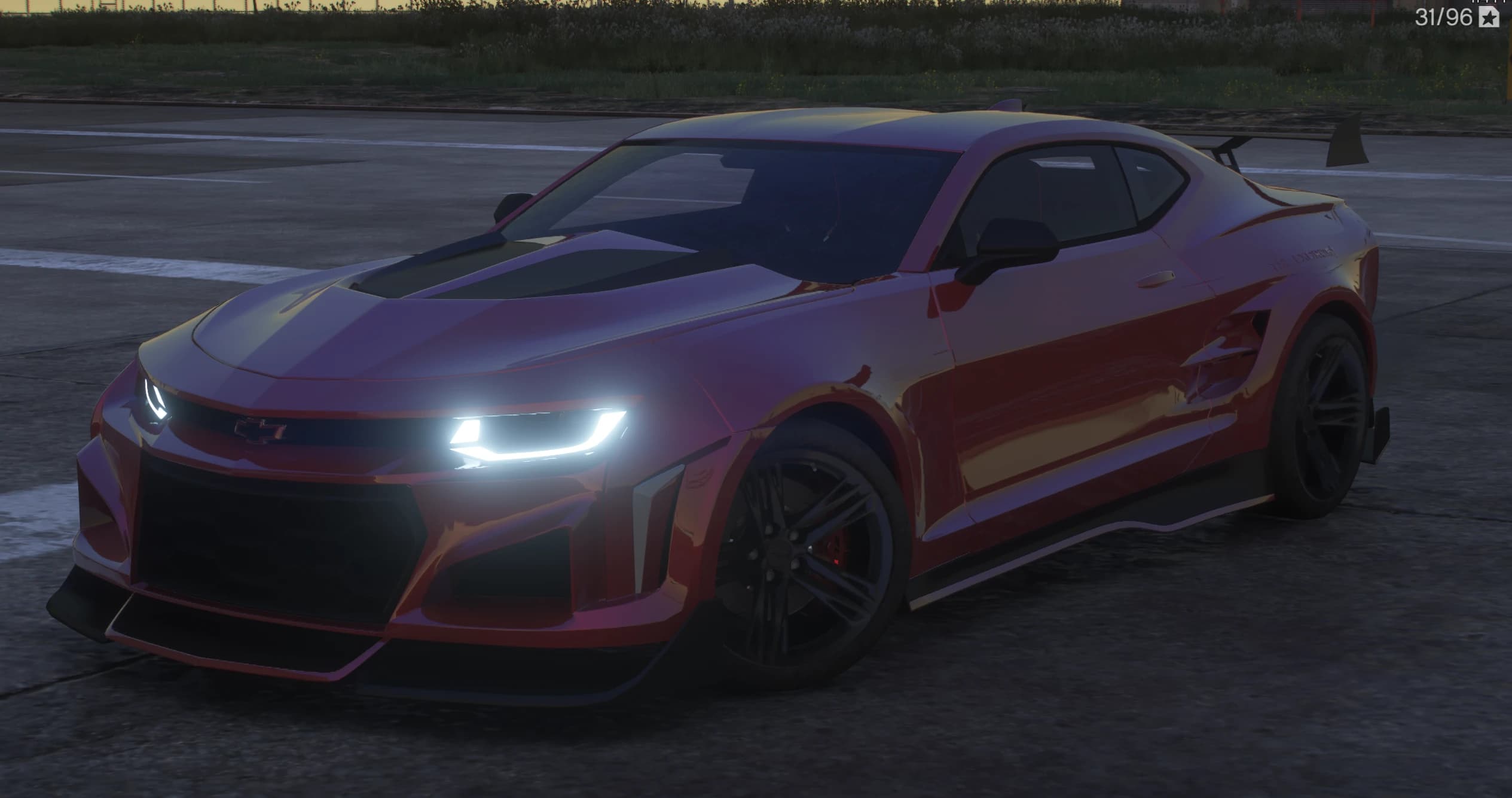 Front three quarter view of the red Camaro ZL1 at dusk with LED headlights lit, black hood insert and a canard equipped splitter