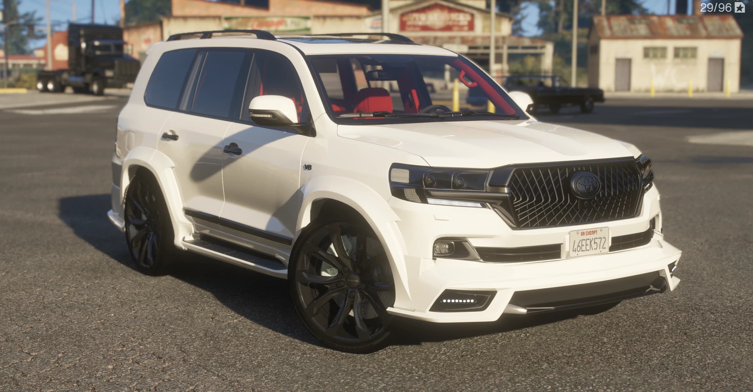White Toyota Land Cruiser 200 with a Wald body kit and red interior, front three-quarter view at a rural gas station