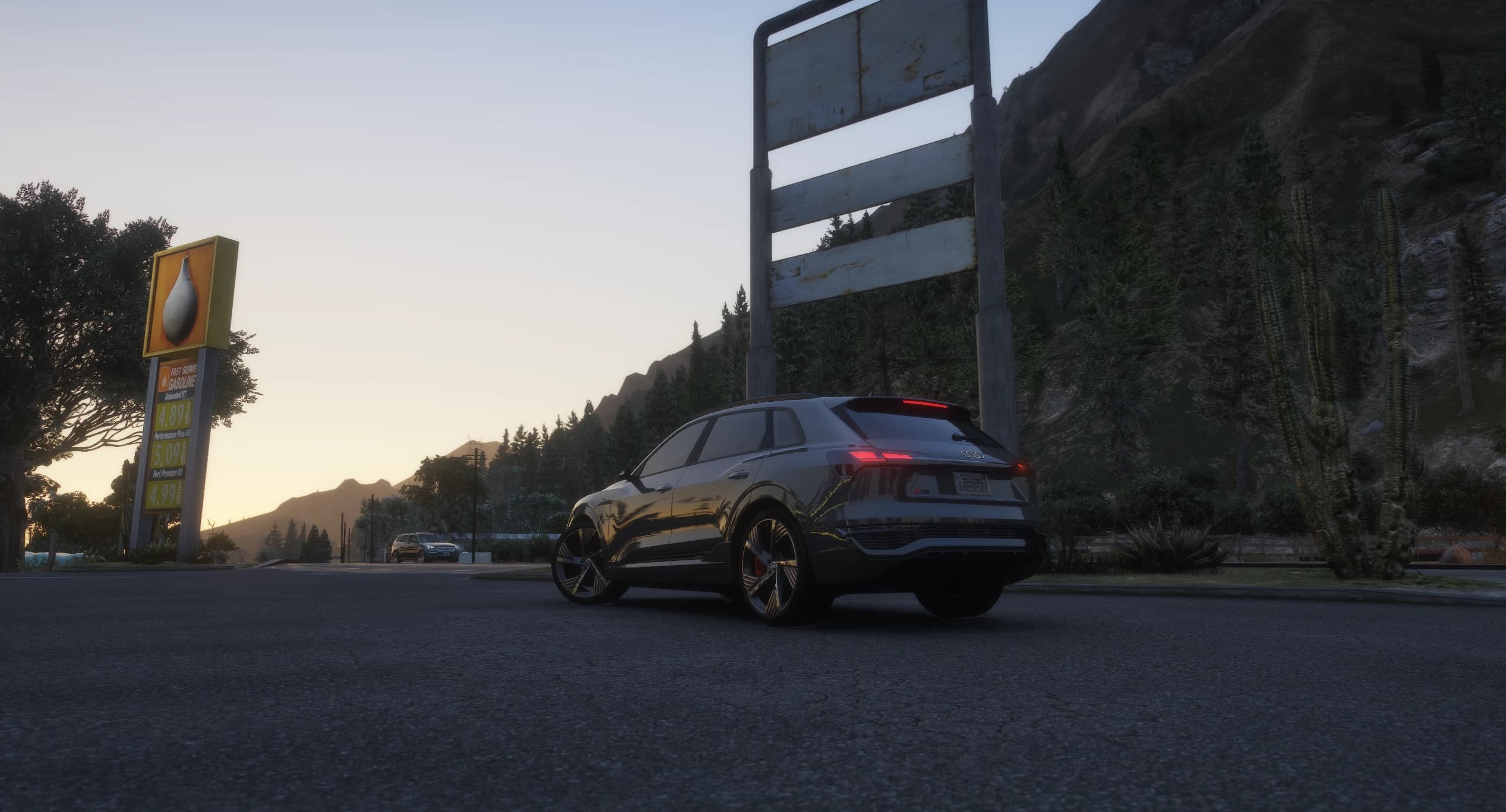 Low rear angle of the Q8 E-Tron parked beside a rural petrol station sign at dusk, with the mountains and cacti of Blaine County behind it