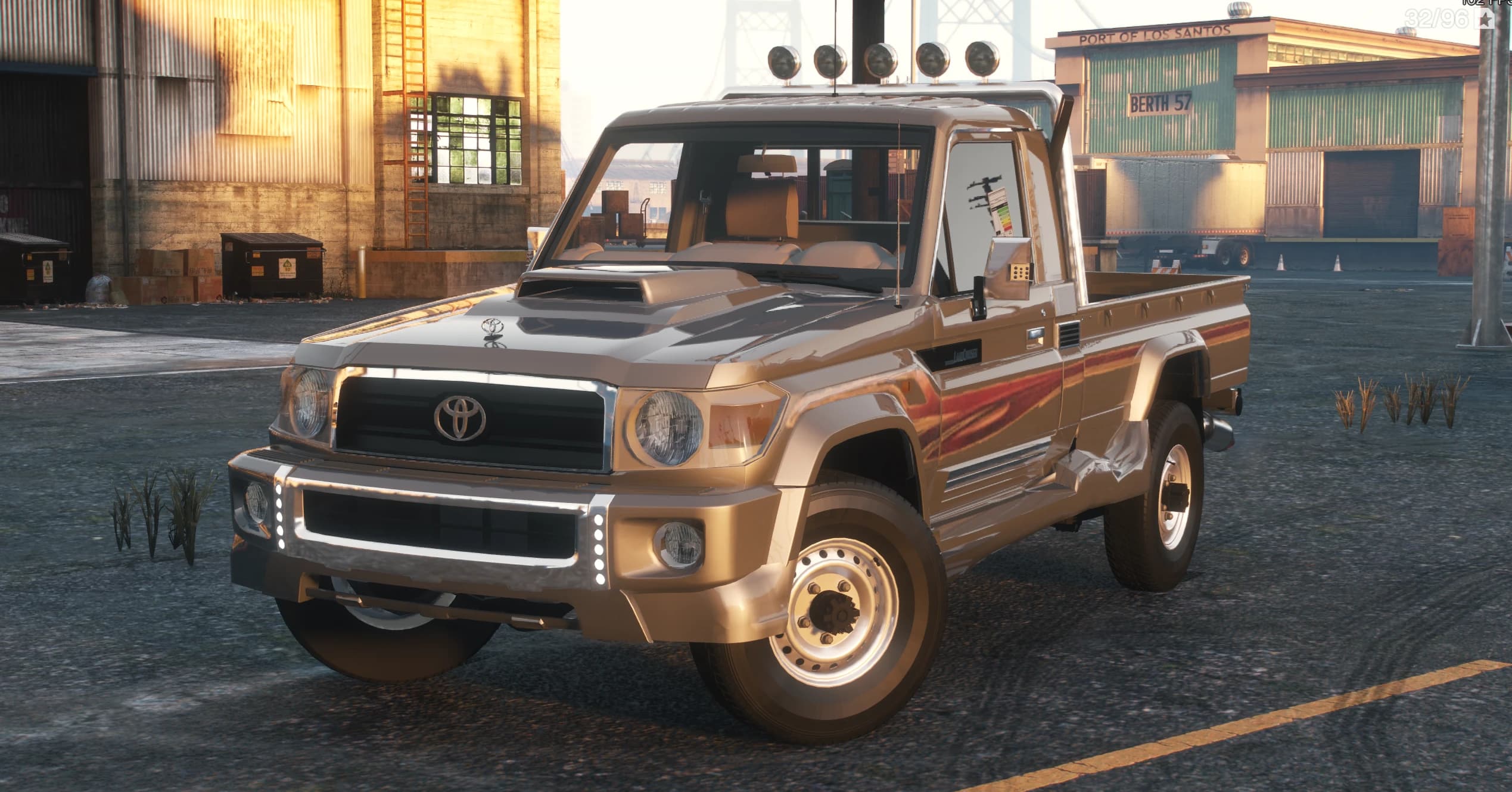 Front three quarter view of the beige Land Cruiser 79 pickup at the docks with five roof spotlights, hood scoop, chrome bumper and side stripe decals