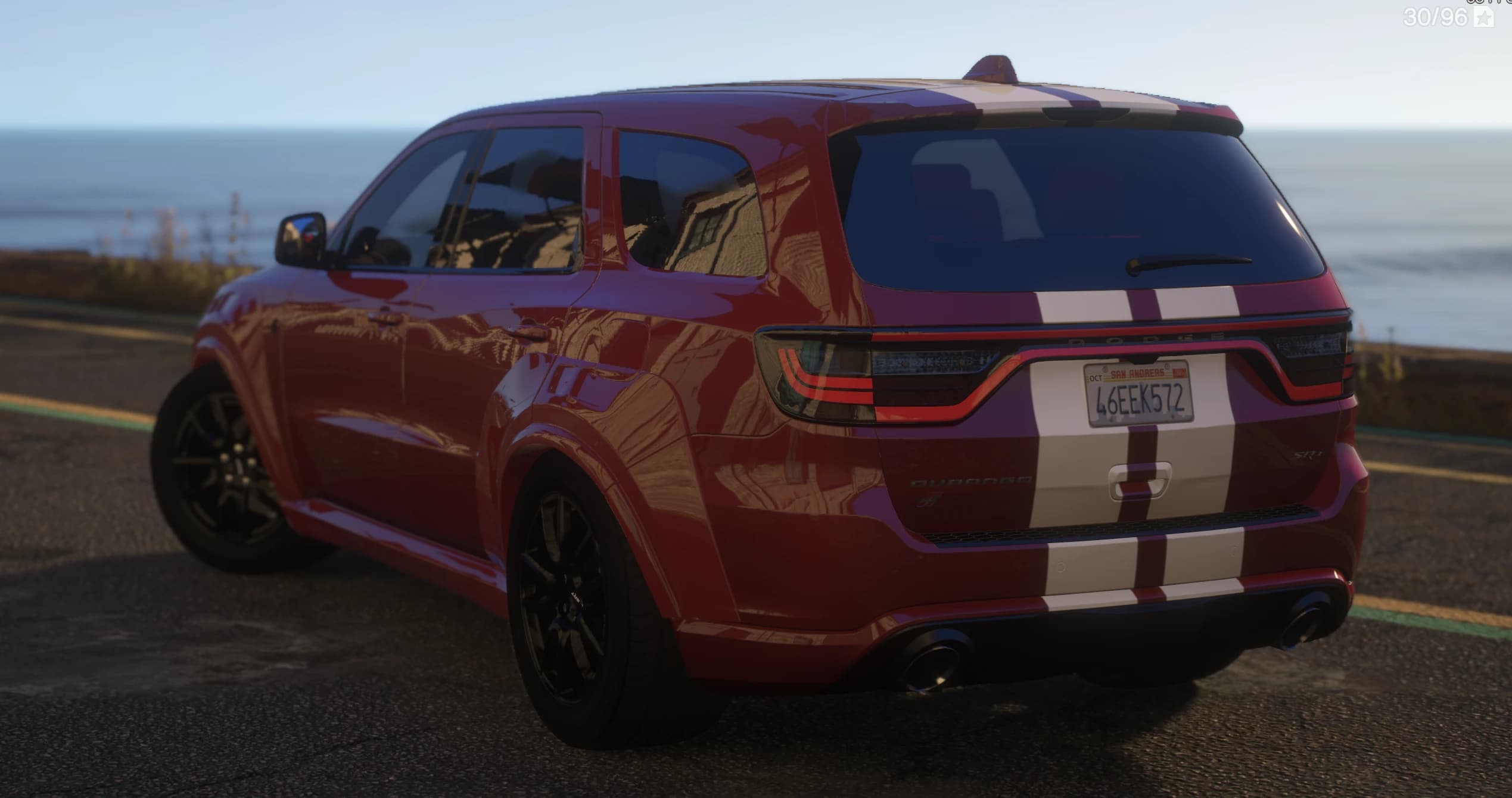 Rear three-quarter of the red Durango on a coastal road, showing the full-width LED light bar with 'DODGE' lettering, the white stripes over the tailgate, dual exhausts and a San Andreas plate reading 46EEK572