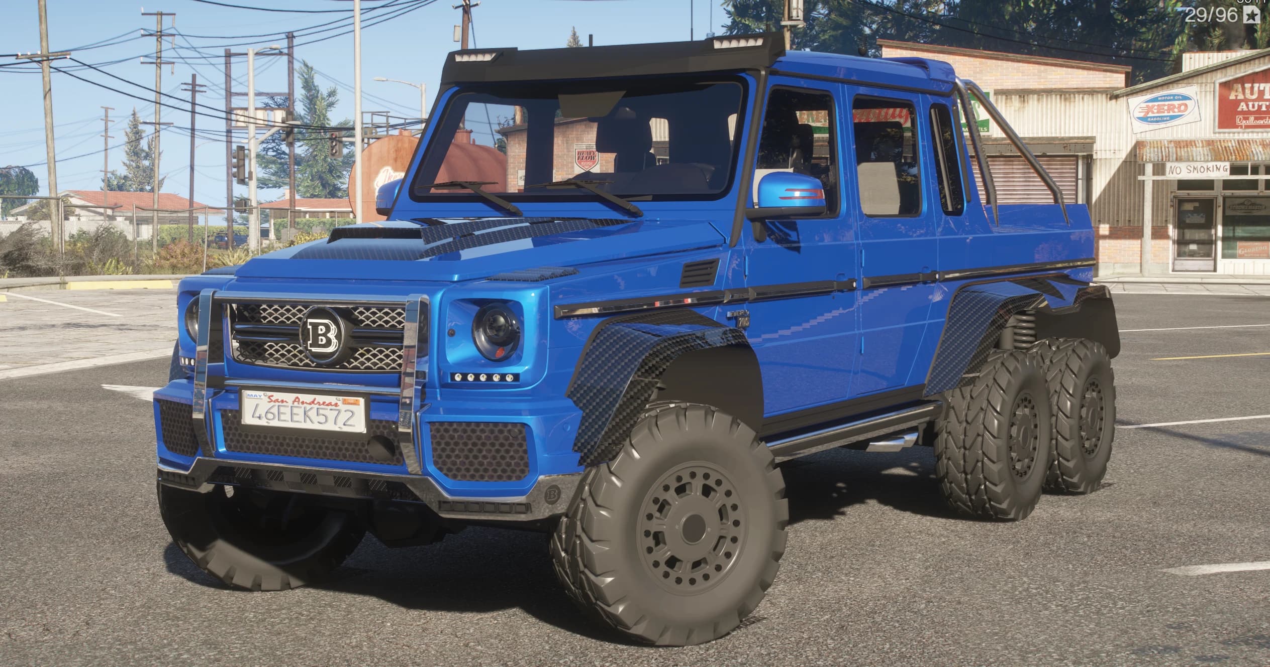 Blue Brabus 700 G63 AMG 6x6 pickup with Brabus B grille badge, bull bar and six off-road wheels, front three-quarter view at a rural gas station
