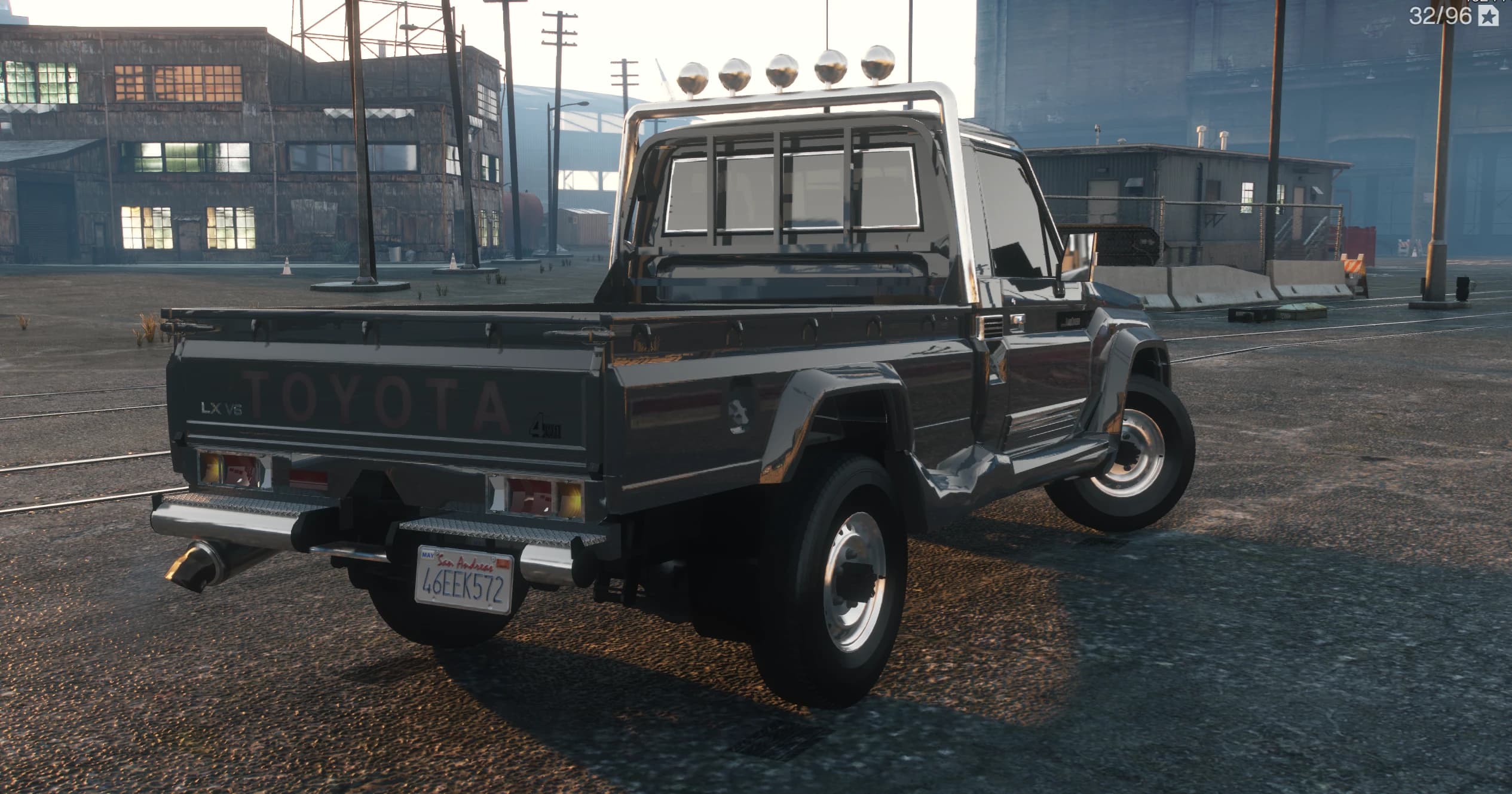 Rear three quarter view of the dark grey variant with TOYOTA lettering on the tailgate, LX V6 badge, chrome bumper steps and the lit roll bar lights