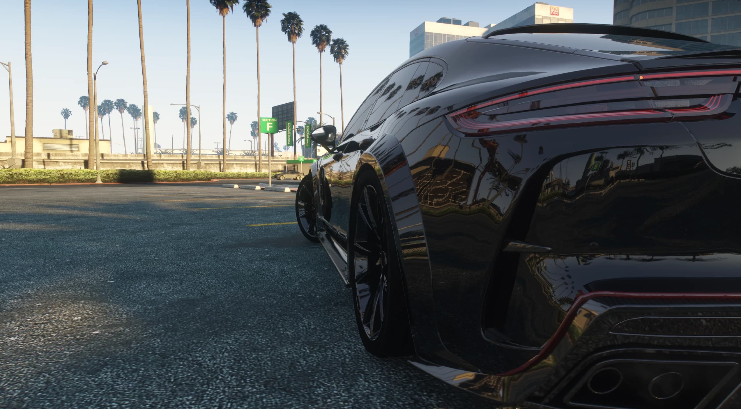 Low rear close up under palm trees showing the taillight strip, the vents cut into the rear bumper and the gloss black paint reflecting the street
