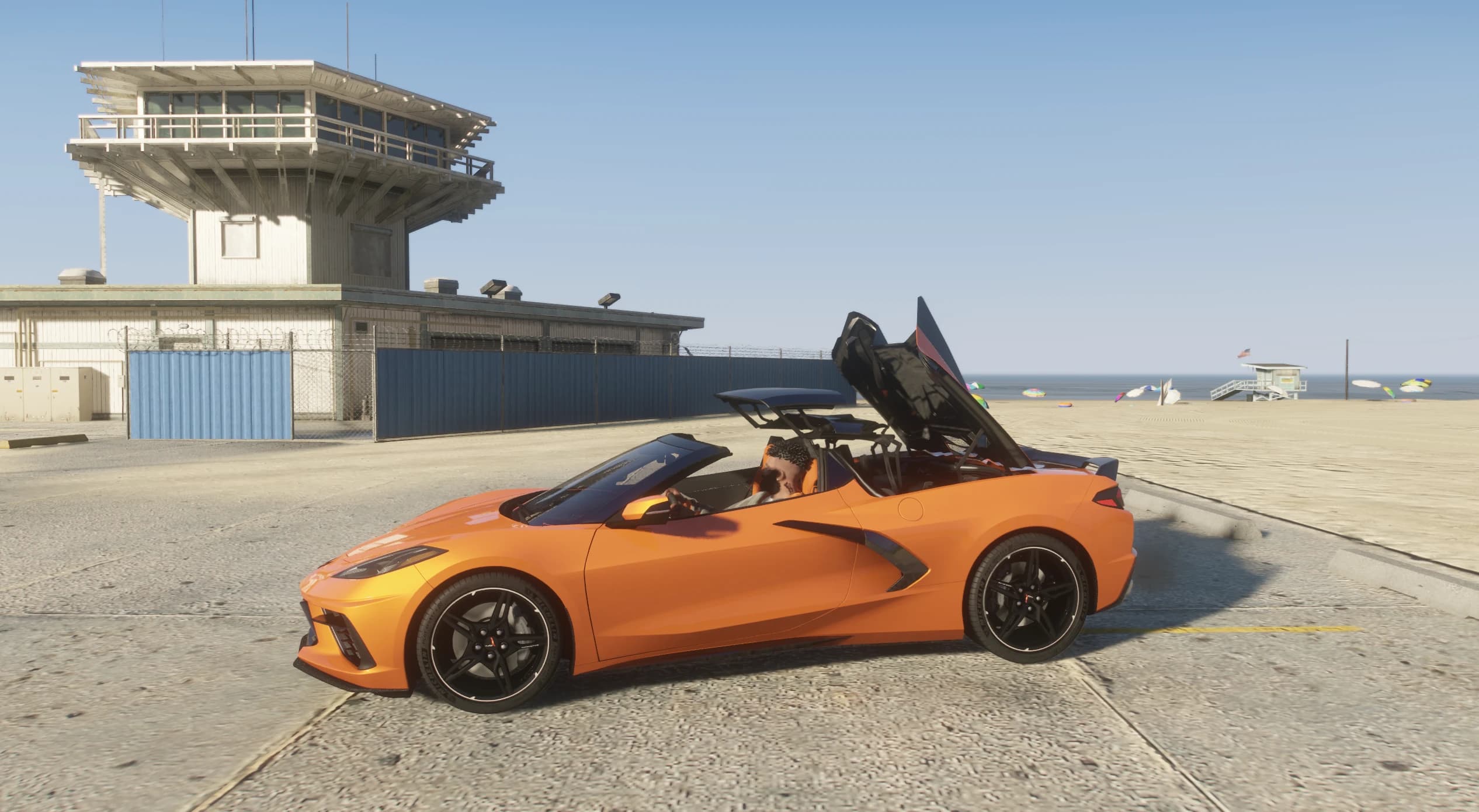 Side view of the convertible with the retractable hardtop caught mid-fold behind the seats, next to a beach watchtower