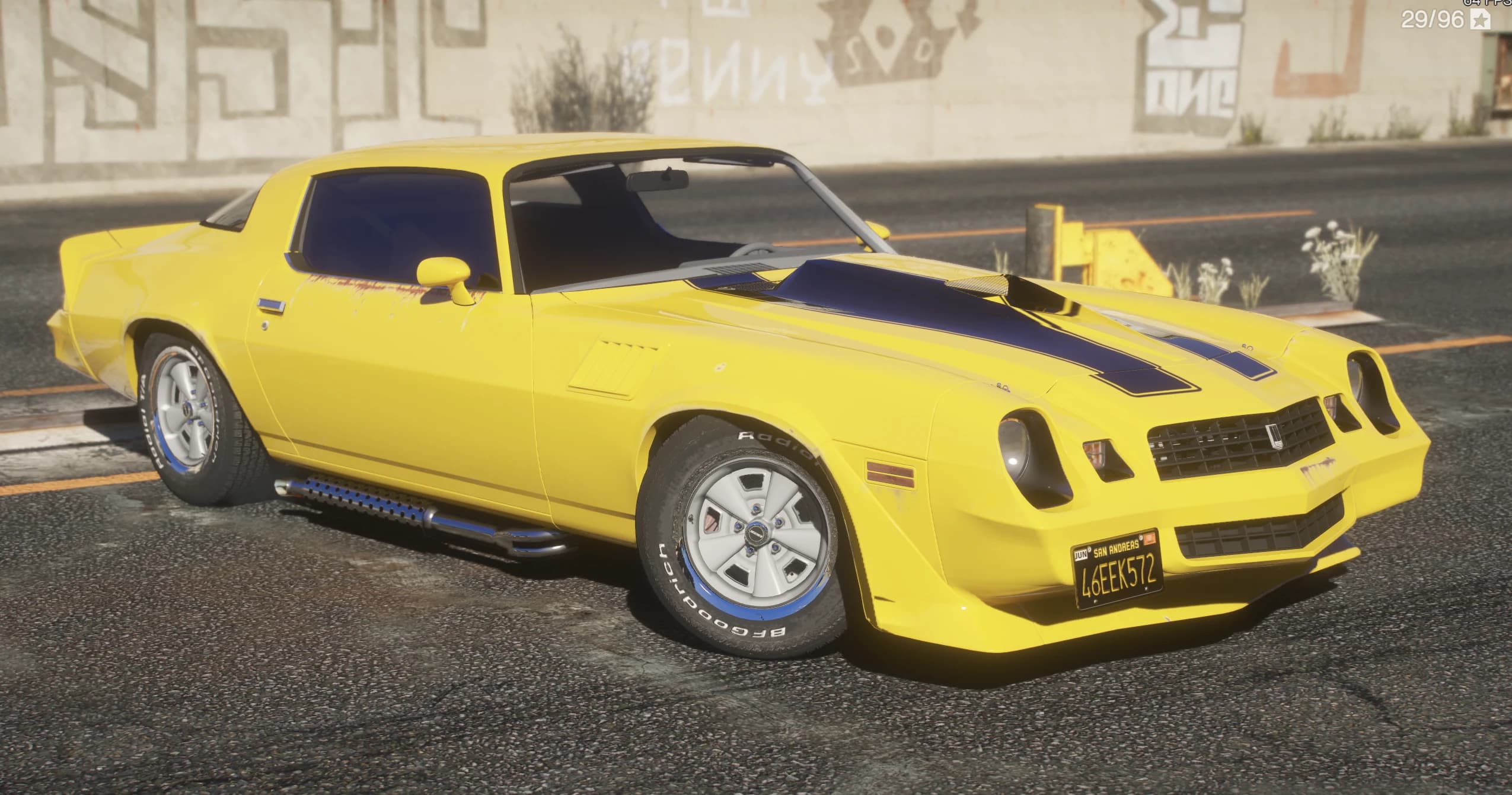 Front three quarter view of the yellow Camaro Z28 with black hood stripes and BFGoodrich white letter tires by a graffiti wall