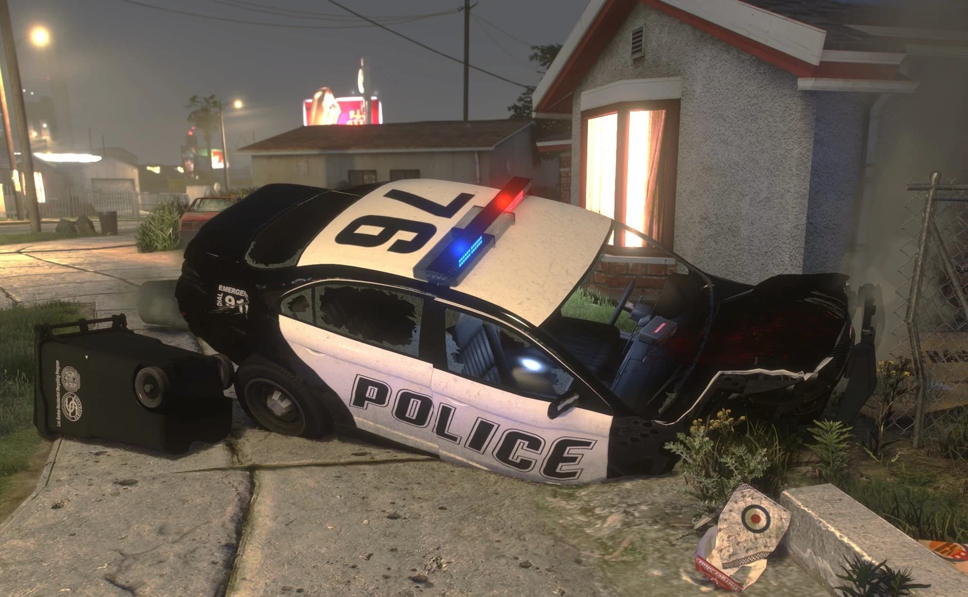 Police cruiser wrecked against a house wall at night: the front end is torn open, the doors are buckled and every window is shattered