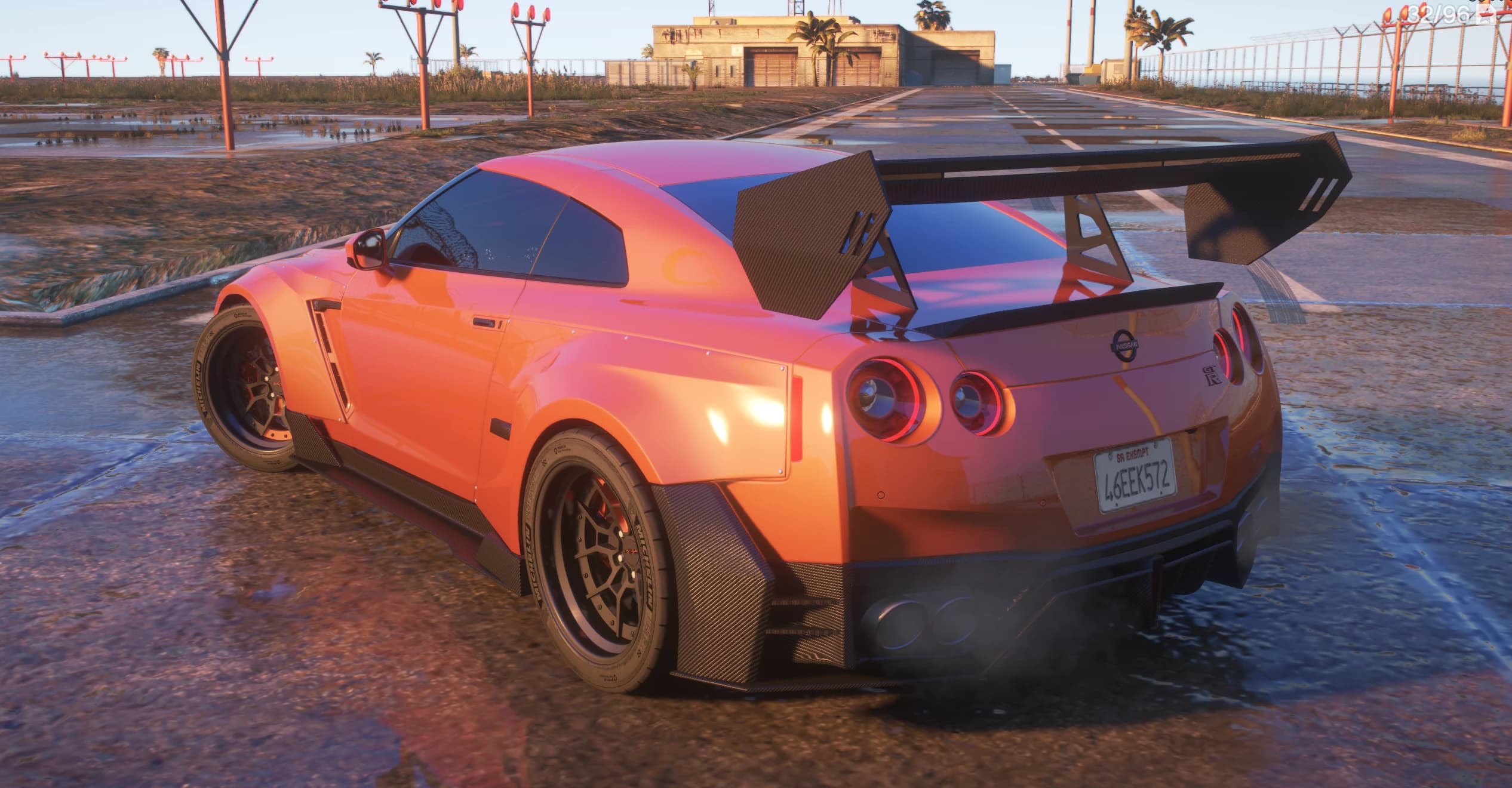 Rear three quarter view at a sunset airfield showing the swan neck carbon wing, four round taillights and riveted widebody arches