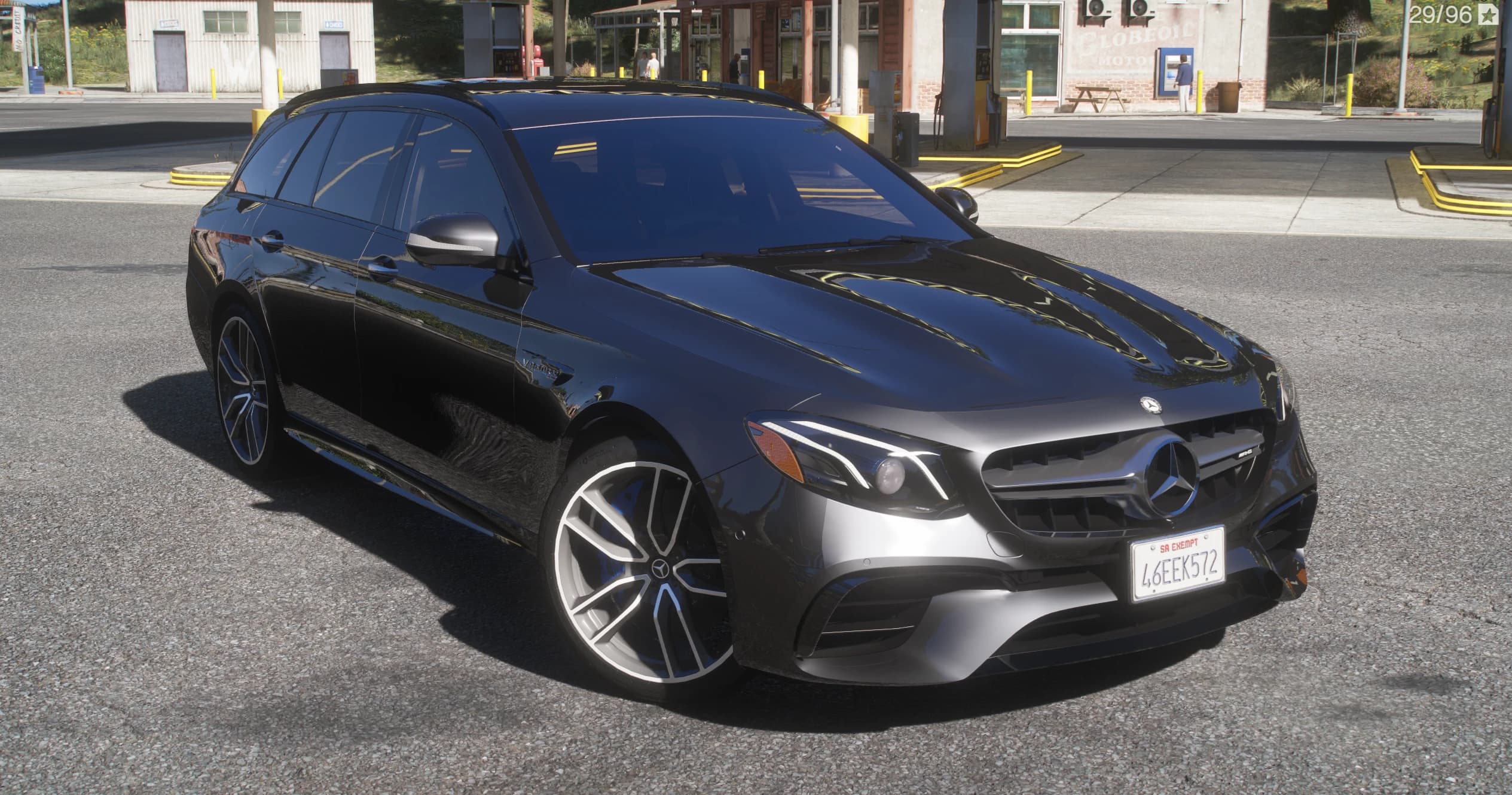 Black Mercedes-AMG E63 S W213 Estate, front three-quarter view with the Panamericana grille, the V8 Biturbo fender badge and multi-spoke AMG wheels with blue calipers, at a gas station