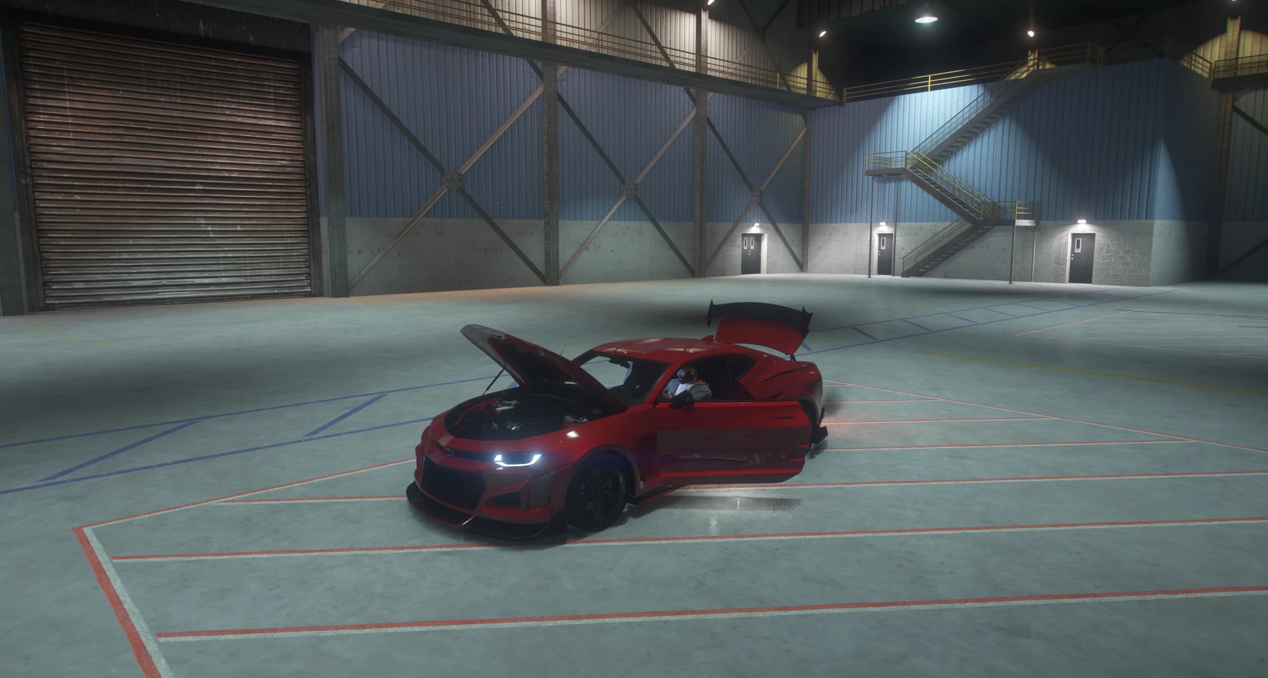 The red Camaro inside a hangar with the hood open over the V8, both doors open and the trunk lid raised under the wing