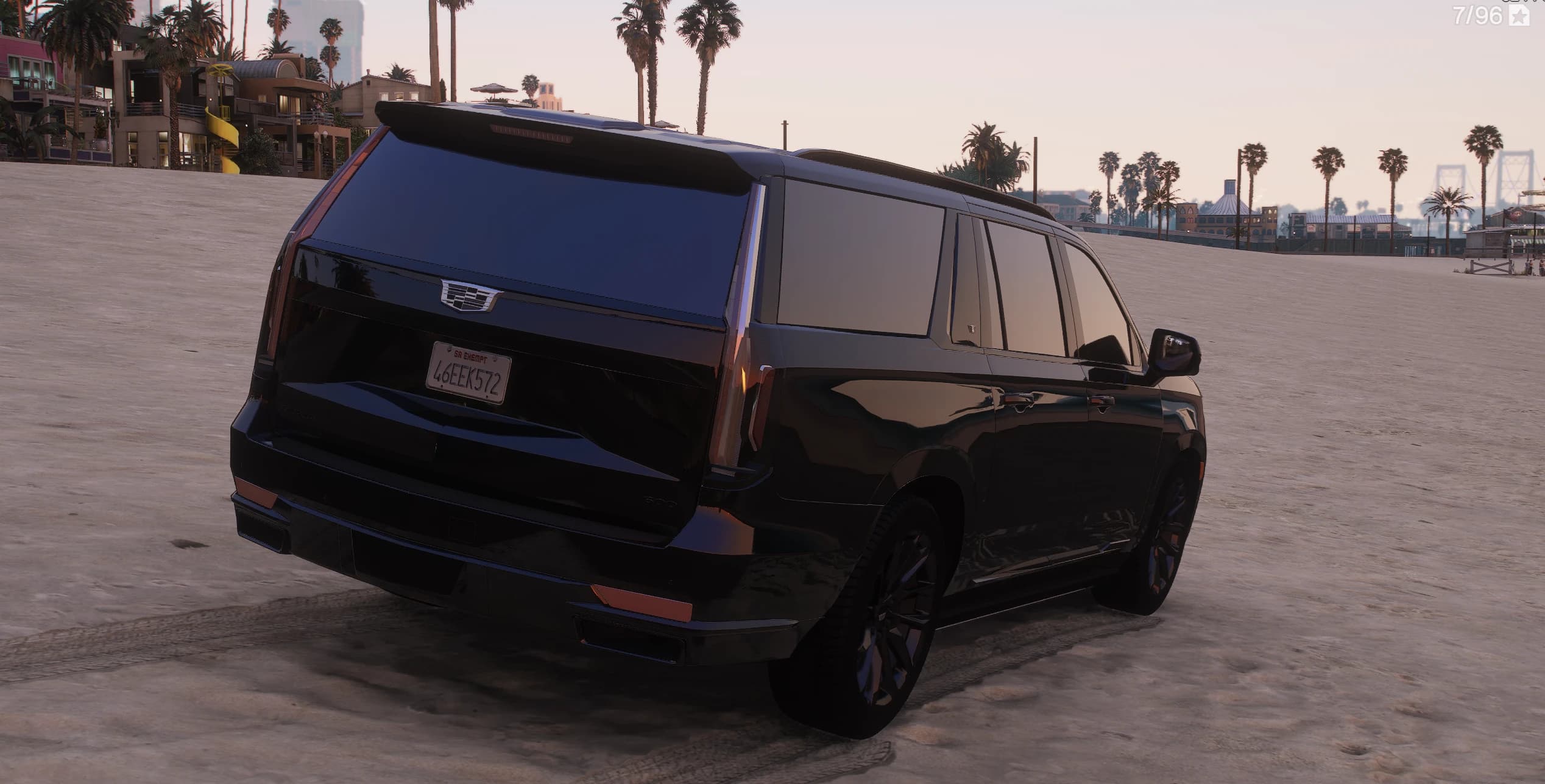 Rear three-quarter of the black Escalade on the beach, with the roof spoiler, the Cadillac crest on the tailgate and the San Andreas plate 46EEK572, palm trees and the pier behind it