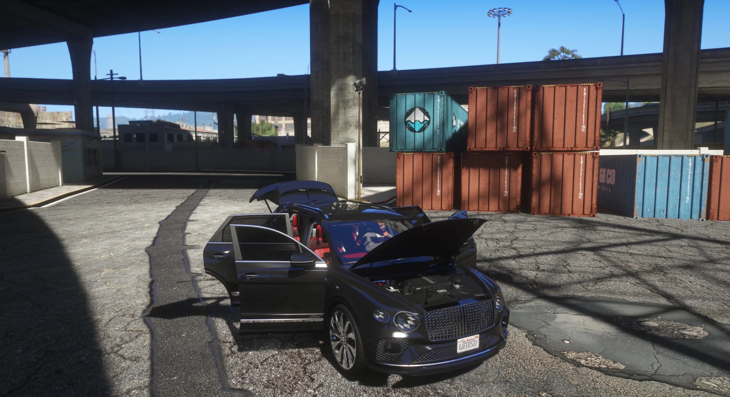 The Bentayga in a container yard with the hood, all four doors and the tailgate open, showing the engine bay and the red and black cabin