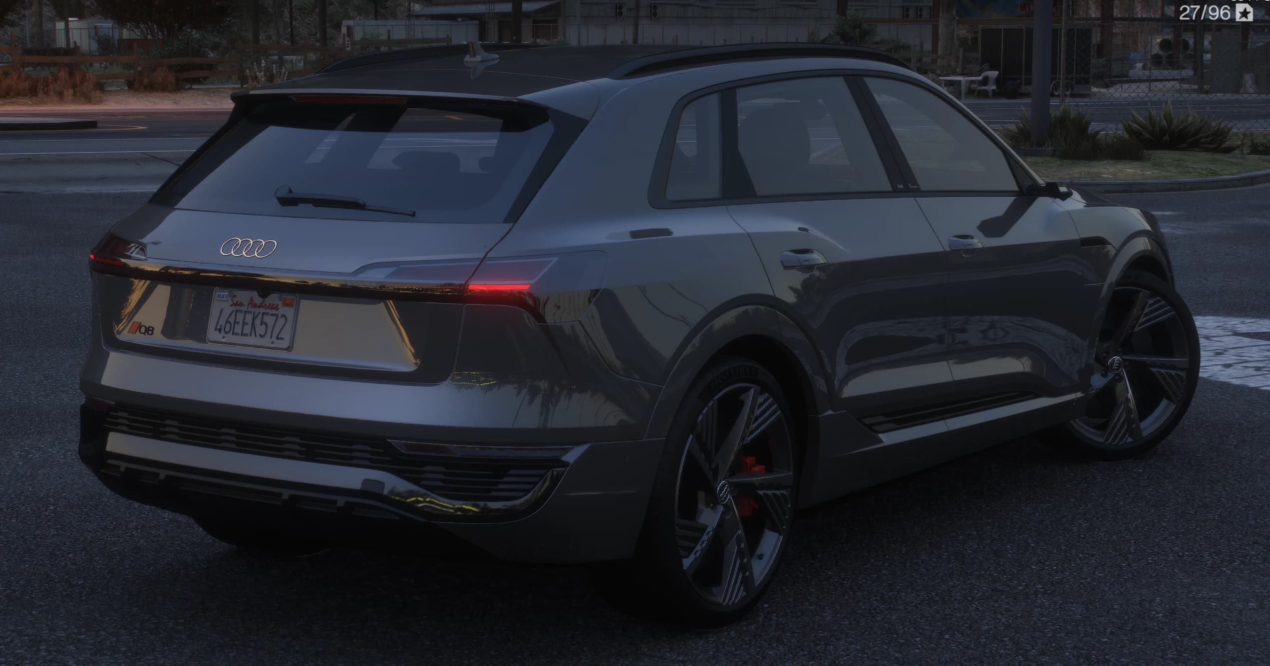 Rear three-quarter of the grey Q8 E-Tron with the roof spoiler, the four-ring badge and the red Q8 lettering on the tailgate, the full-width tail light bar lit and a San Andreas plate