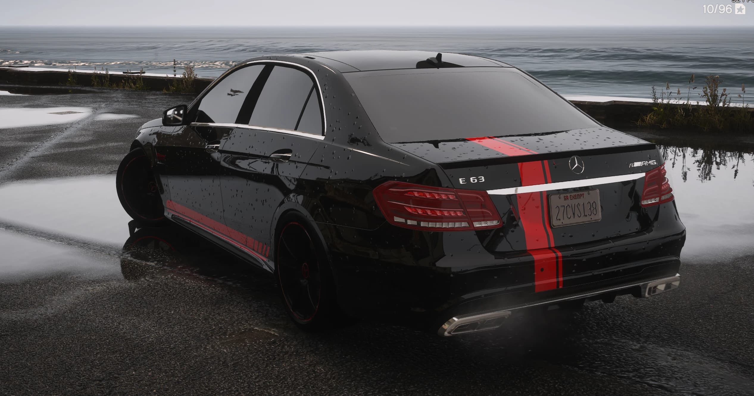 Rear three-quarter of the black E63 S AMG showing the E 63 and S AMG badges, red stripe and quad exhaust by the sea