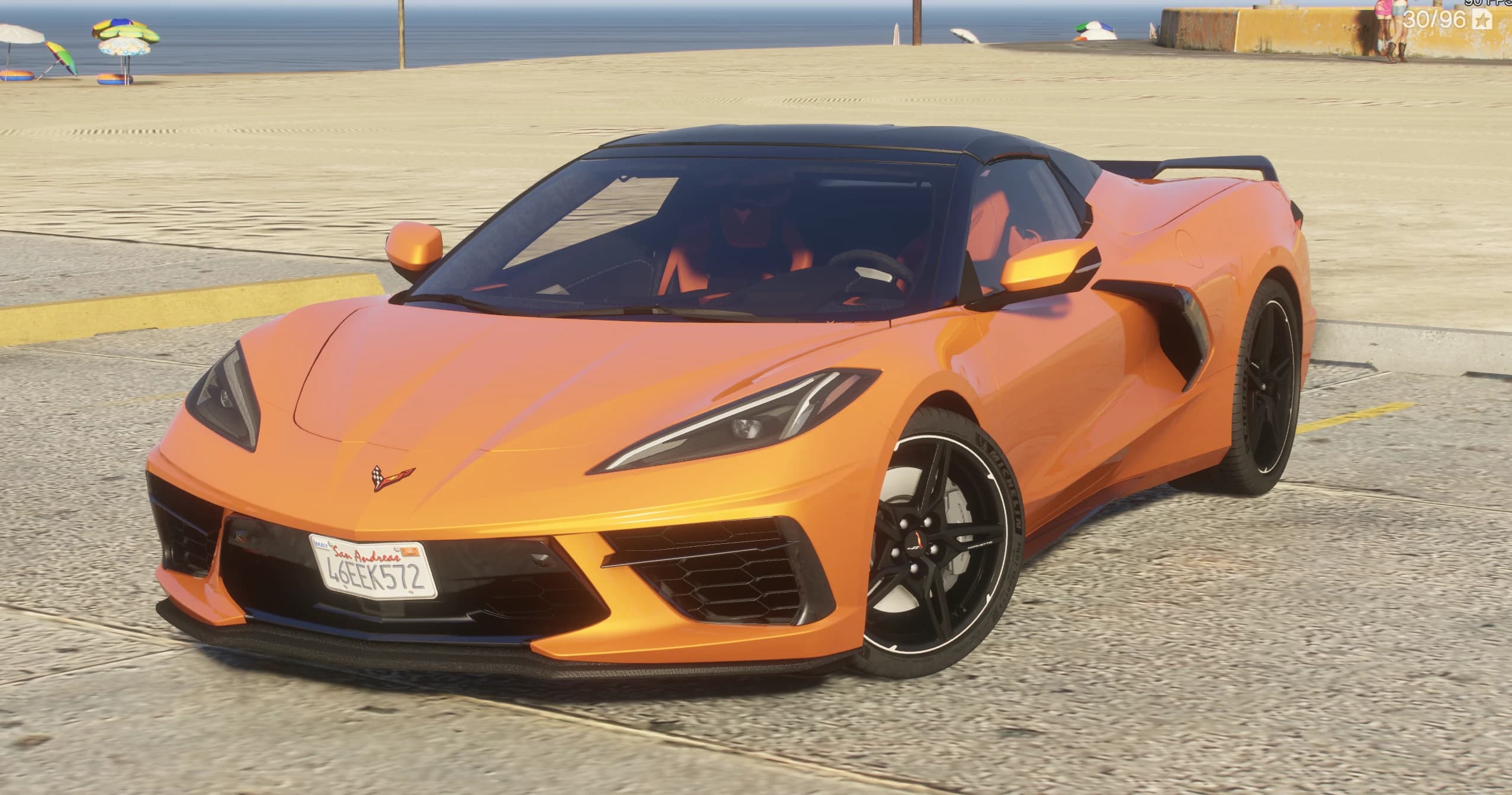 Front three quarter view of the orange Corvette C8 convertible with the black hardtop closed, parked on the beach promenade