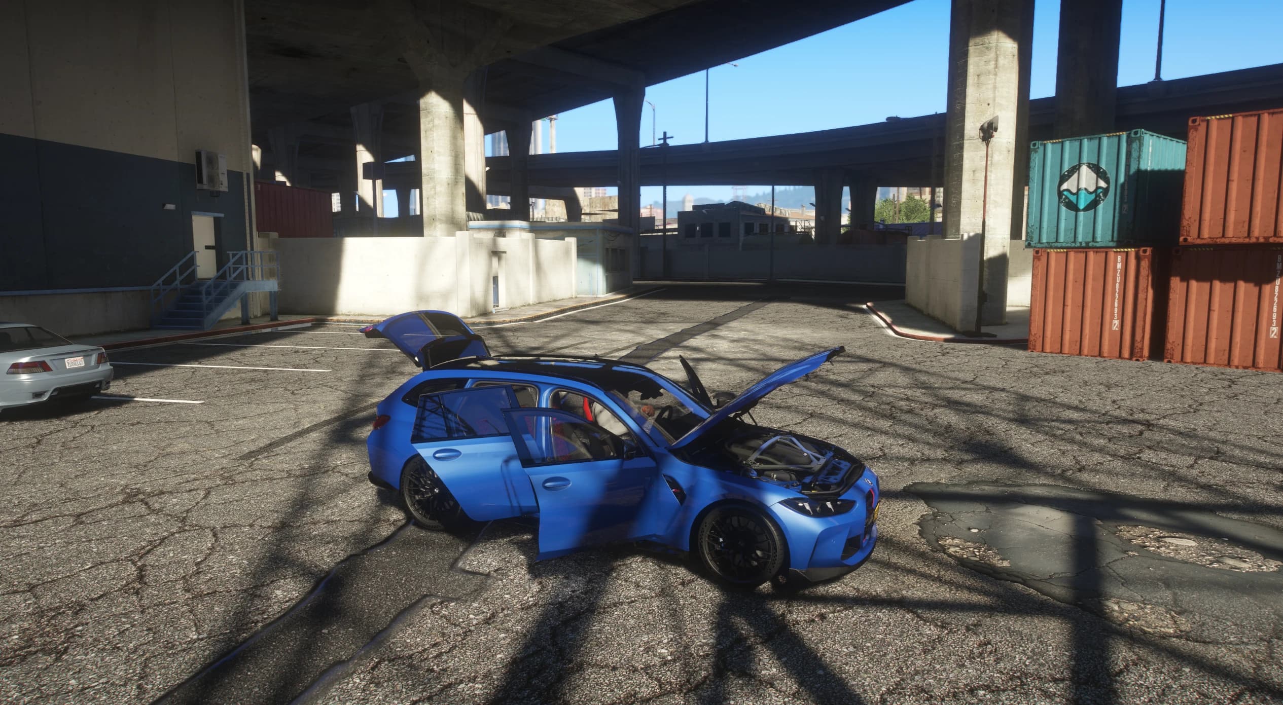 The M3 CS Touring in blue with the hood, all four doors and the tailgate open under a motorway overpass