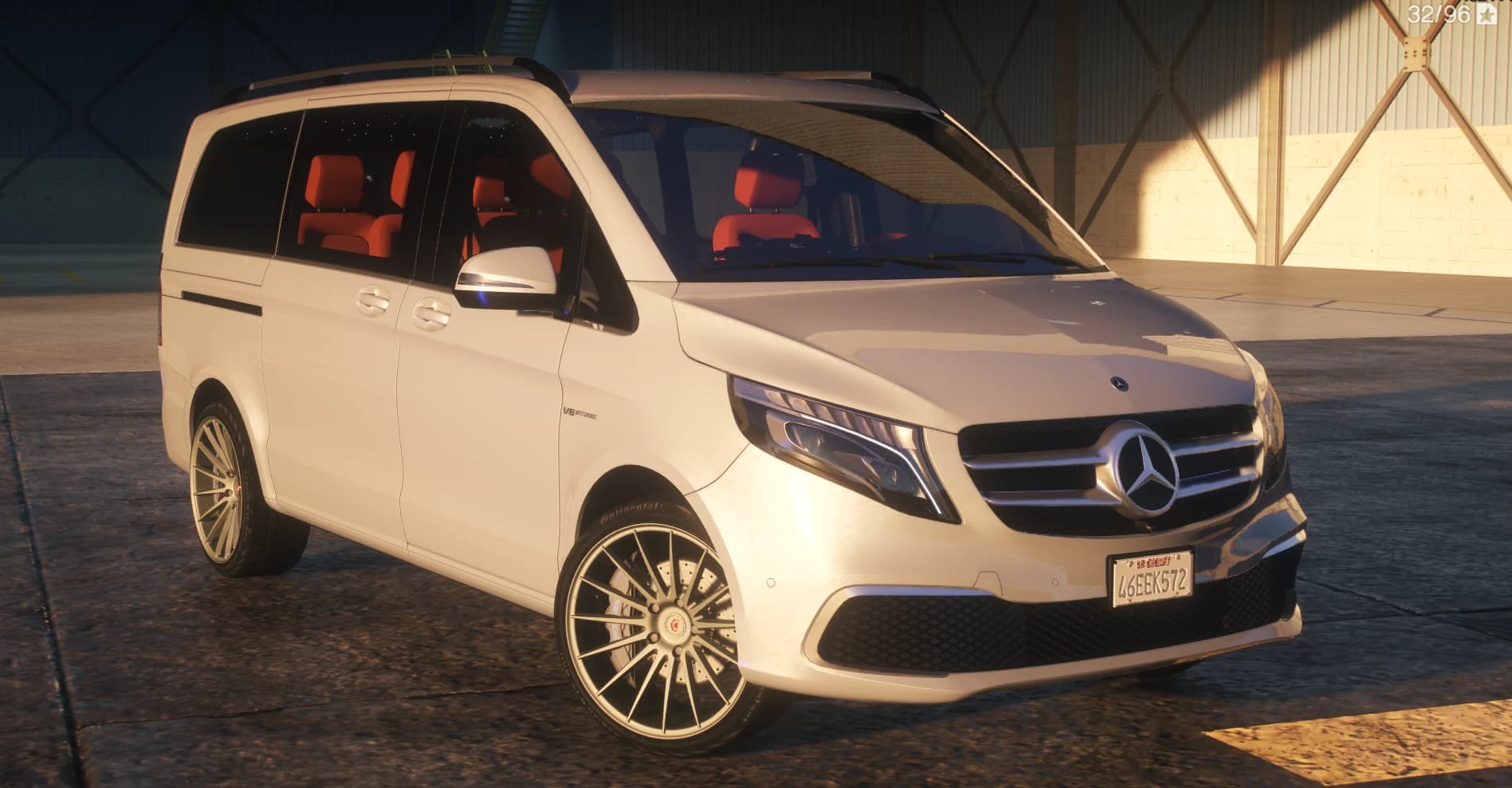 Front three quarter view of the white V-Class in a hangar with the AMG style grille, V8 Biturbo fender badge, turbine spoke wheels and red seats inside