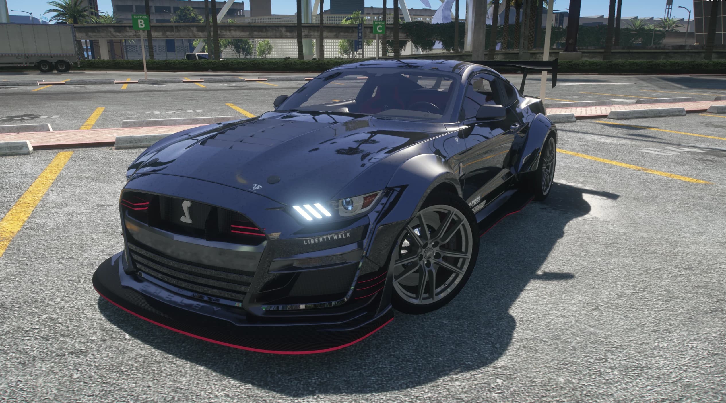 Front three quarter view of the dark blue GT500 with Liberty Walk lettering on the nose, red pinstriped splitter, cobra grille badge and tall GT wing