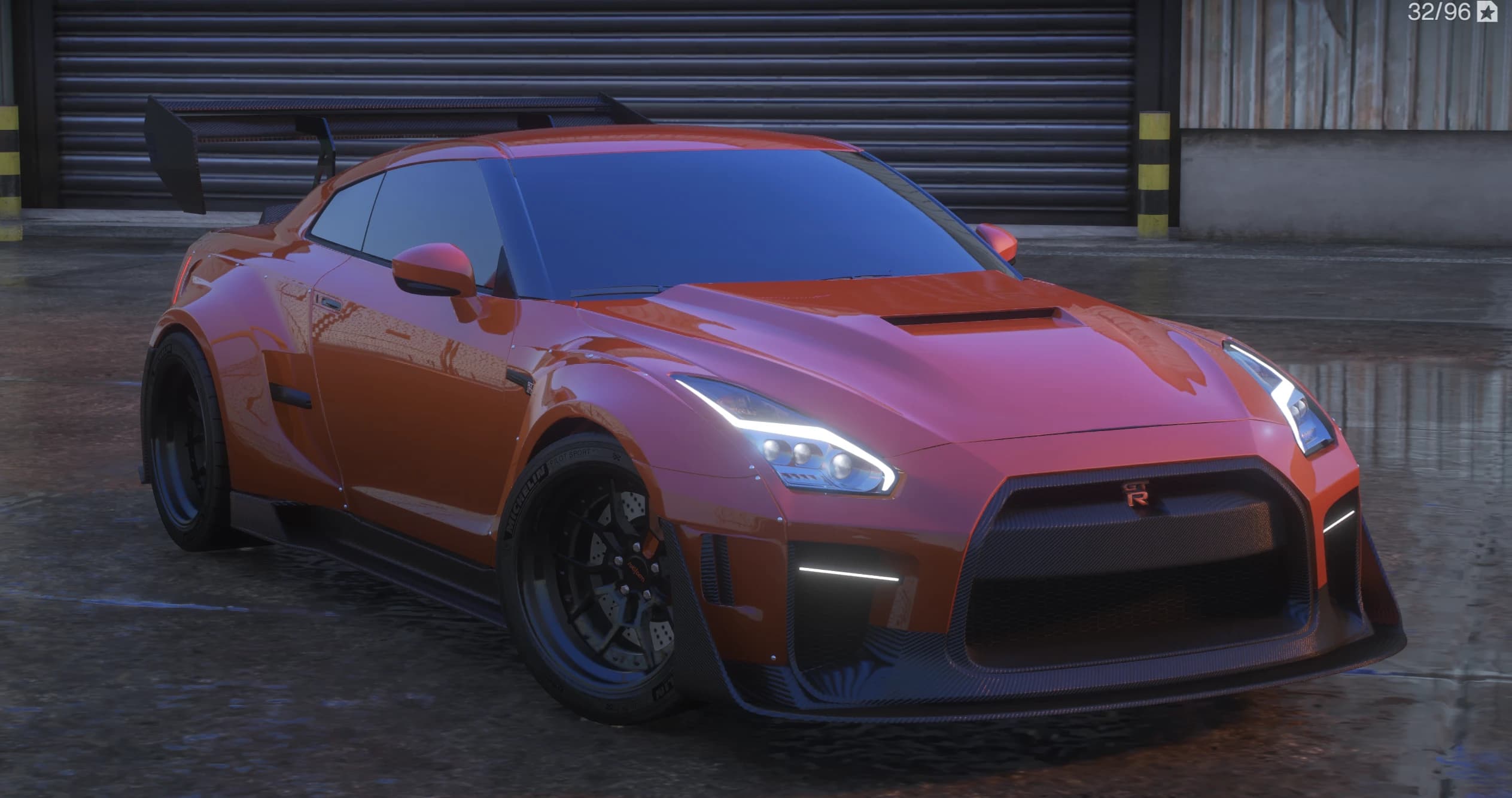 Front three quarter view of the orange widebody Nissan GT-R with carbon canards, vented hood and a tall carbon GT wing in front of a garage shutter