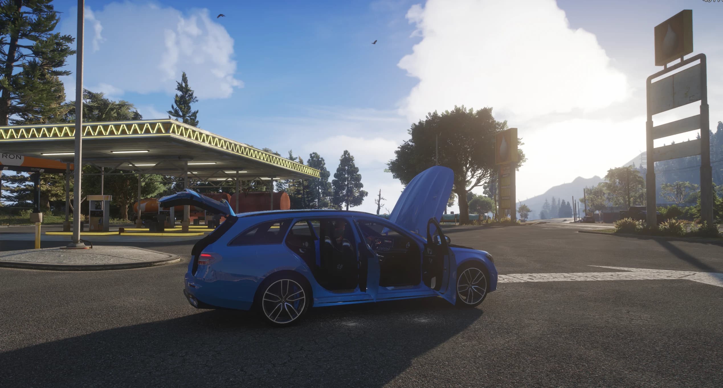 A blue E63 S Estate variant with the doors, bonnet and tailgate open at a gas station, showing the interior and boot