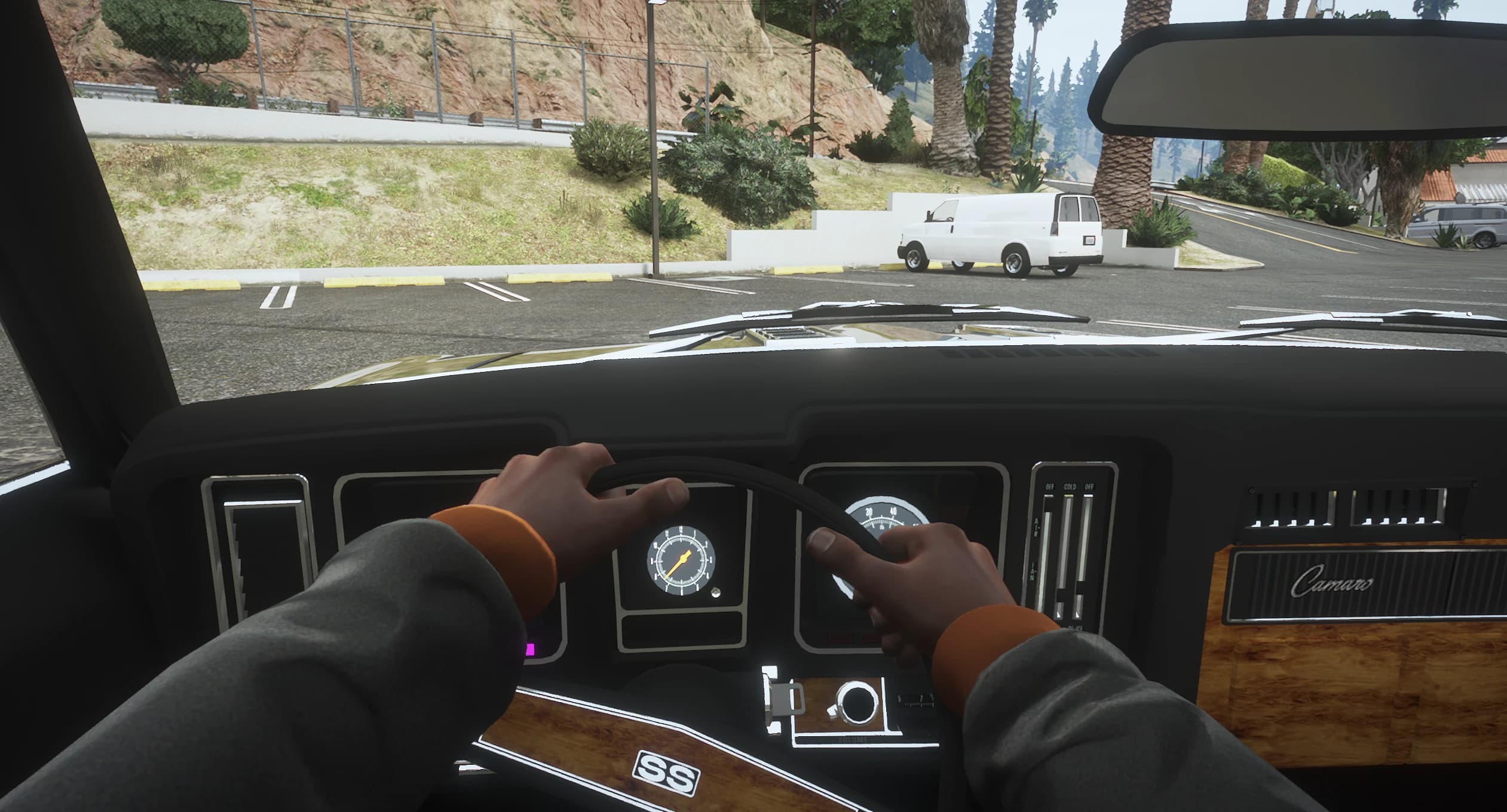 First person view behind the wheel with the woodgrain dashboard, round gauges and the Camaro script on the glovebox