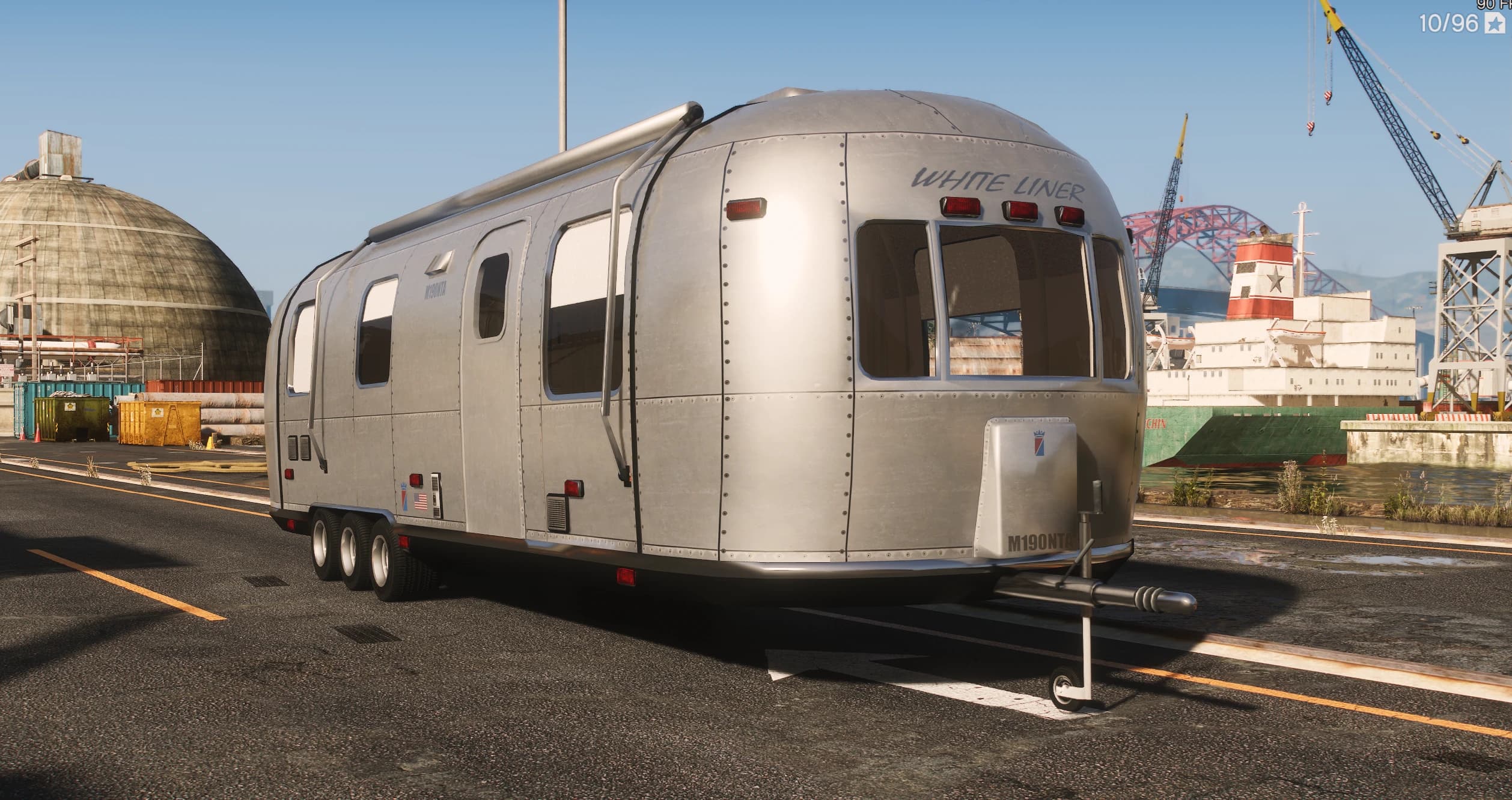 Silver riveted-aluminium Albany White Liner travel trailer with WHITE LINER lettering and a triple-axle chassis, parked at the docks