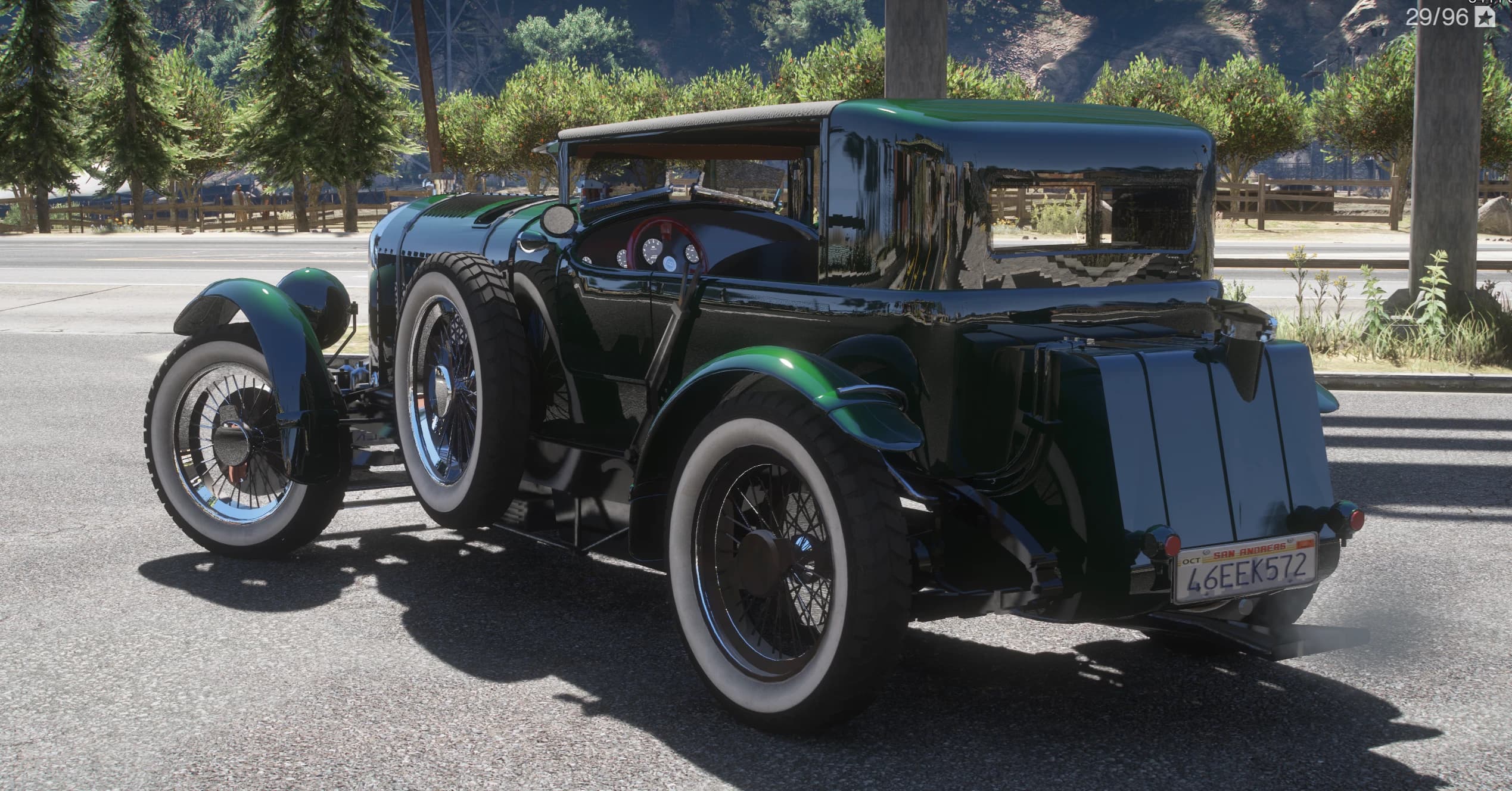 Rear three-quarter of the Bentley with the folded fabric top, the spare wheel and the slab fuel tank at the back on a country road