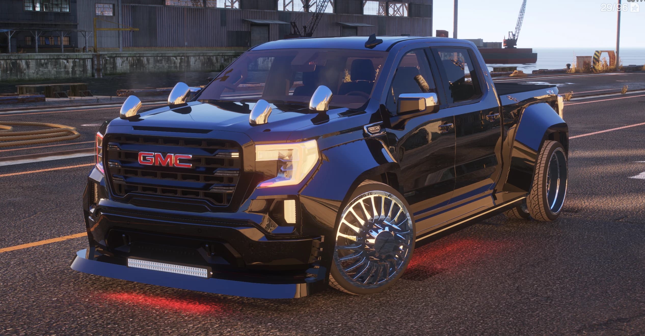 The black GMC Sierra in a shipyard with roof-mounted bullet lights, chrome dually wheels and red underglow