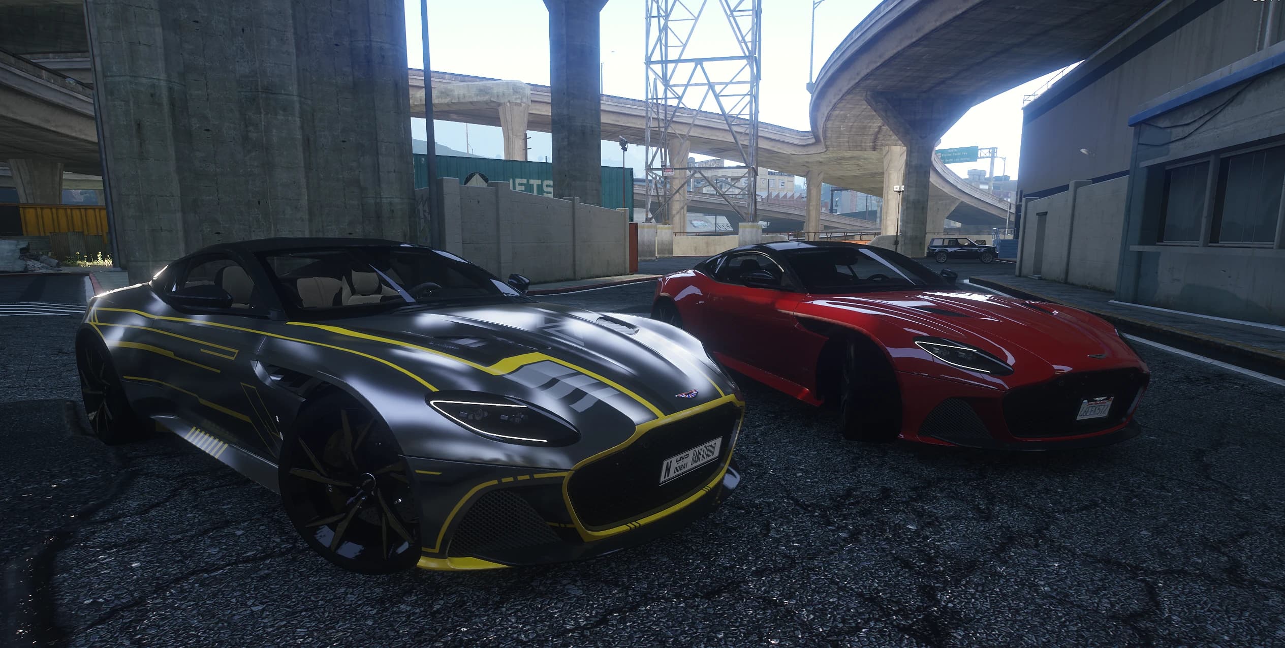 The two DBS Superleggera add-ons parked side by side under a freeway: a gray one with a yellow tron style livery and a plain red one