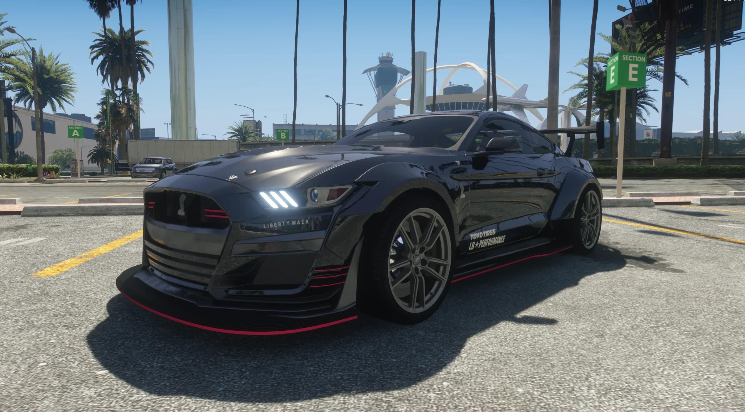 Front view at the airport with lit LED headlights, TOYO TIRES and LB Performance door decals and red trim lines along the kit