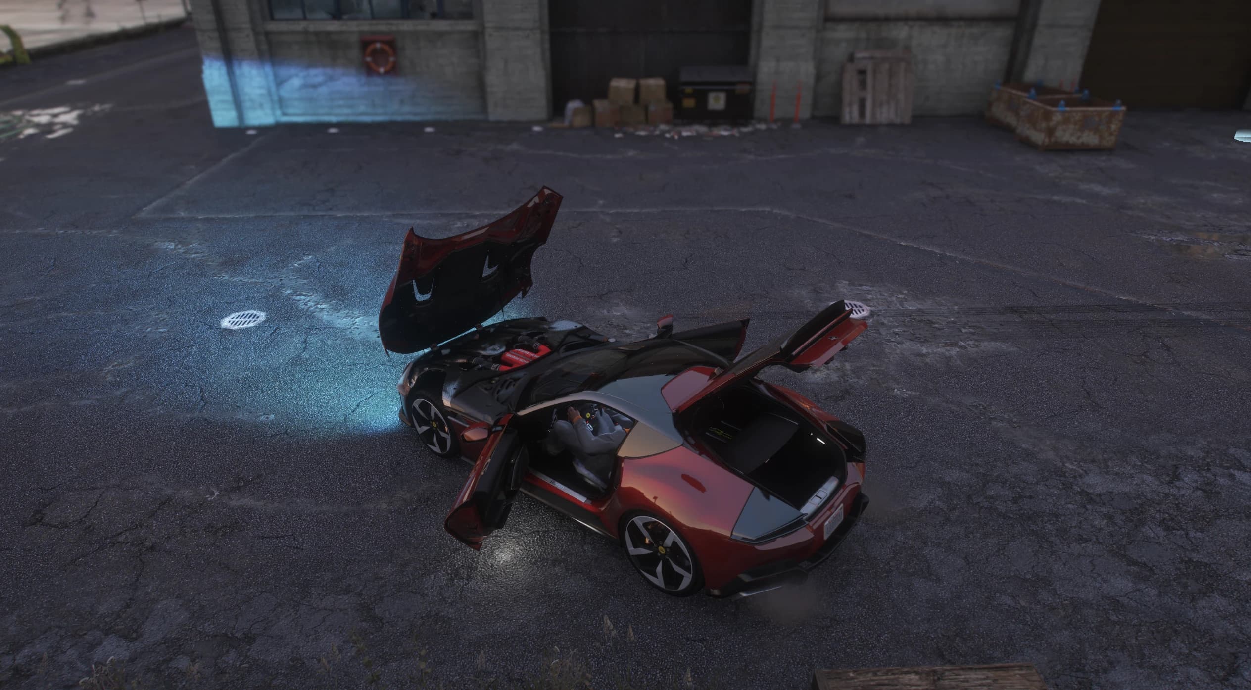 Overhead night shot with the front-hinged bonnet, doors and boot open, exposing the V12 engine with its red cam covers