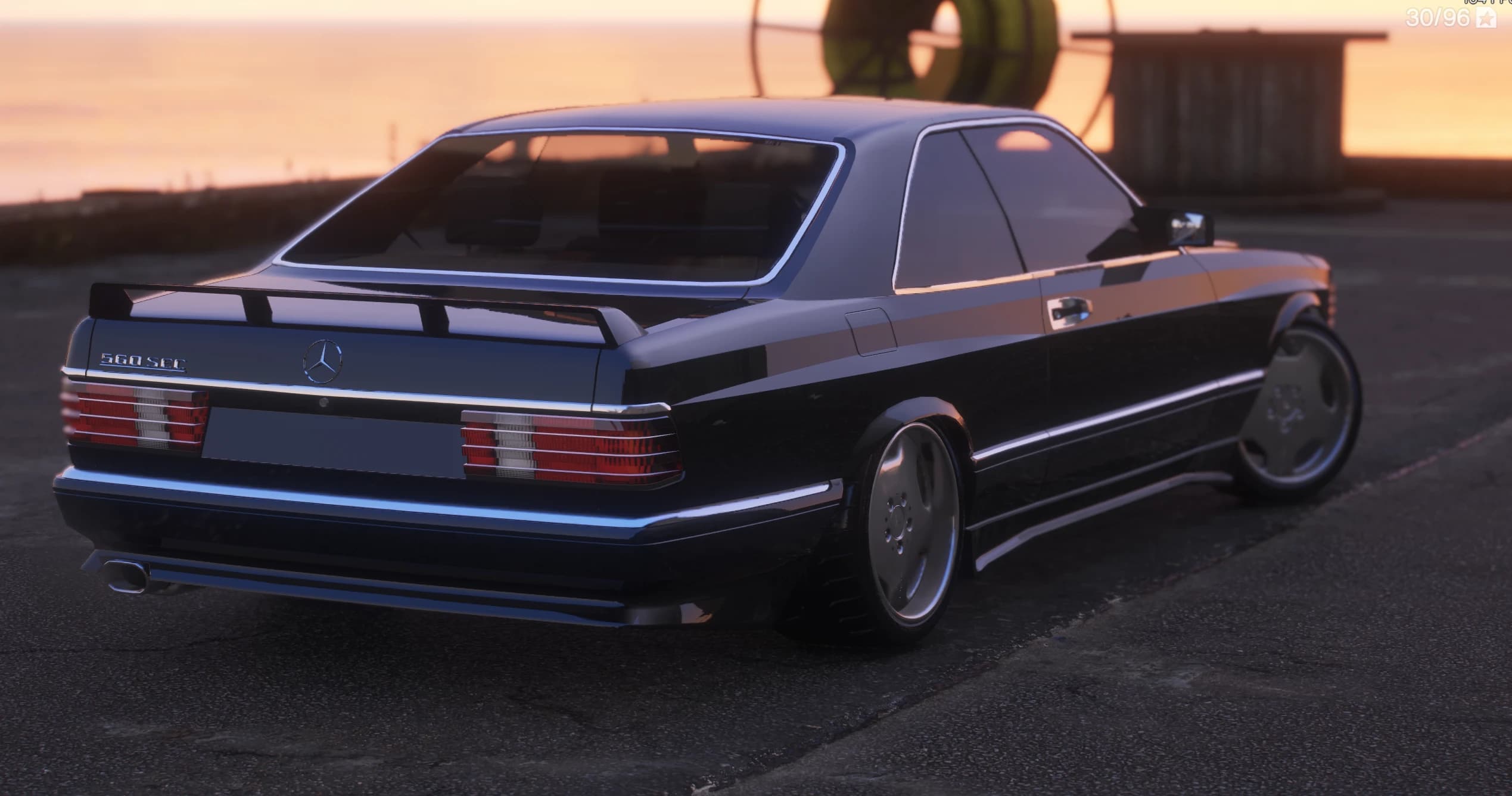Rear three-quarter of the black 560 SEC at sunset by the coast, showing the '560 SEC' boot badge, the three-pointed star, the boot spoiler, the ribbed red taillights and the chrome monoblock wheels