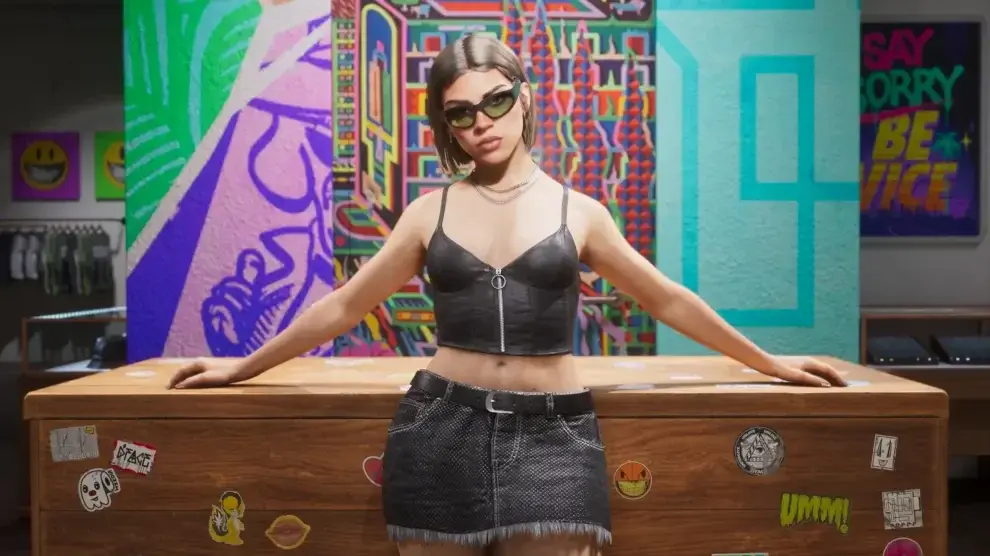 Lucia in sunglasses leaning back against a wooden shop counter covered in stickers, with clothing racks to the left, glass display cases to the right and bright painted murals filling the wall behind her
