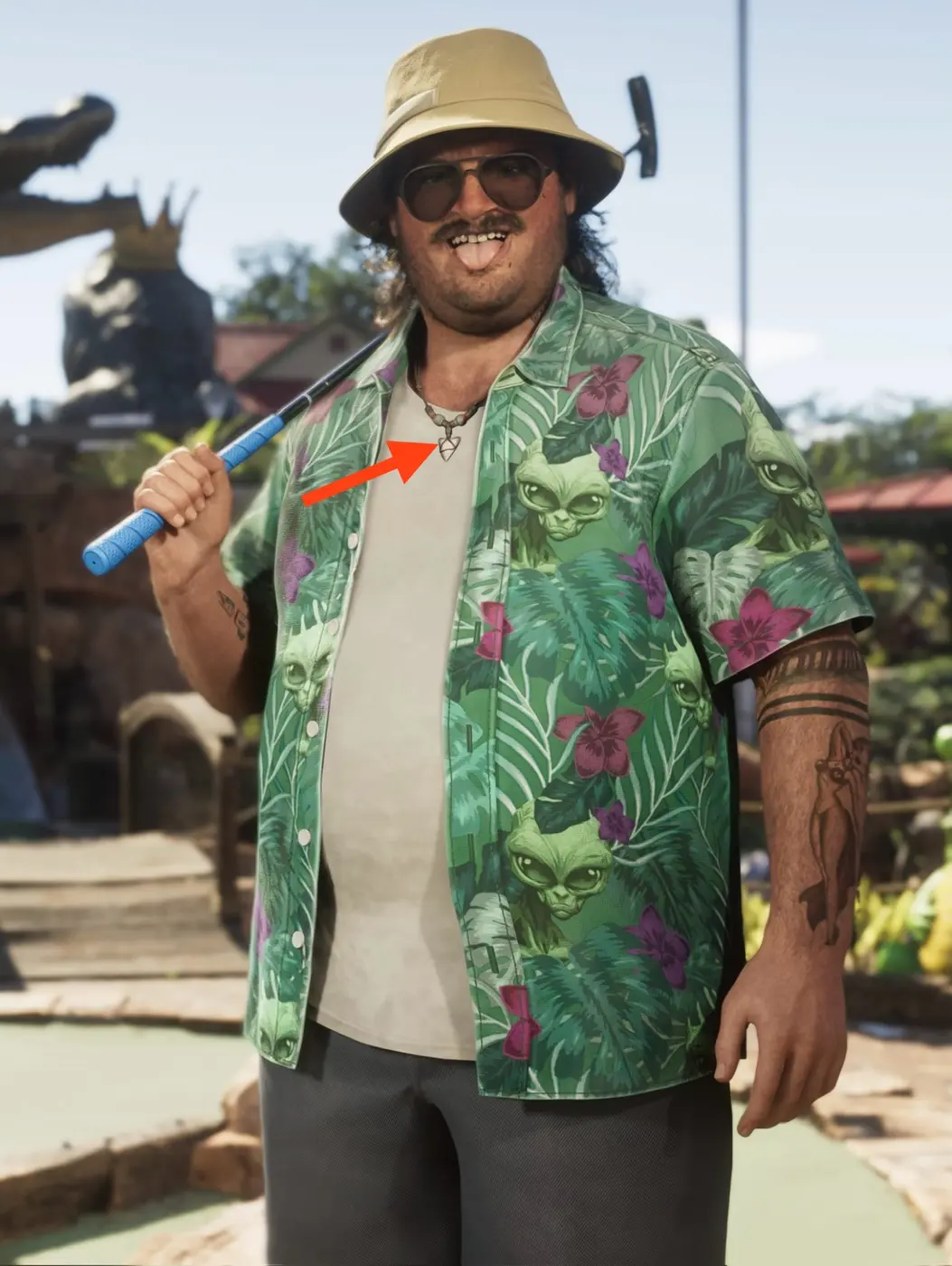 A large GTA Online character in a green tropical shirt covered in alien faces, wearing a bucket hat and sunglasses and holding a golf club, with a red arrow pointing at an hourglass pendant on a beaded necklace matching the one worn by the painter Rae.